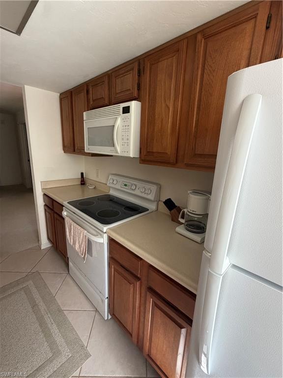 Kitchen featuring wood cabinetry, solid surface countertops, white appliances, and tiled flooring