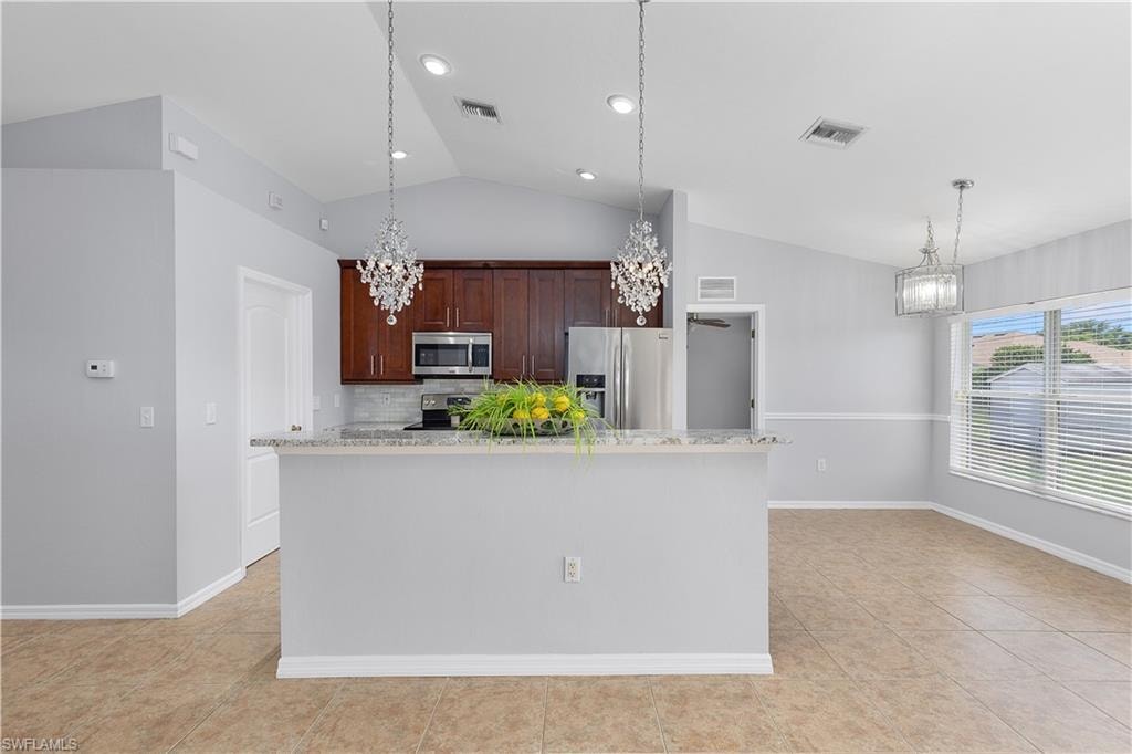 Vaulted ceilings, crystal chandeliers, wood cabinetry, stainless steel appliances, and a breakfast bar with stone-finish countertop
