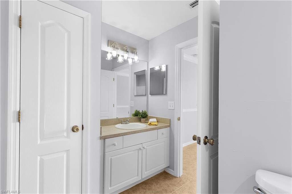 Elegant bathroom vanity featuring white cabinetry with a wood-finish countertop, dual mirrors with integrated lighting, and brushed brass hardware