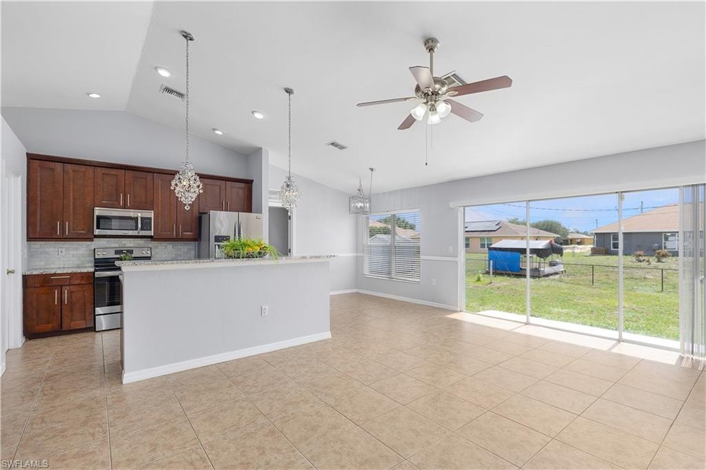 Vaulted ceilings over a kitchen with wood cabinetry, stainless steel appliances, and a tiled backsplash
