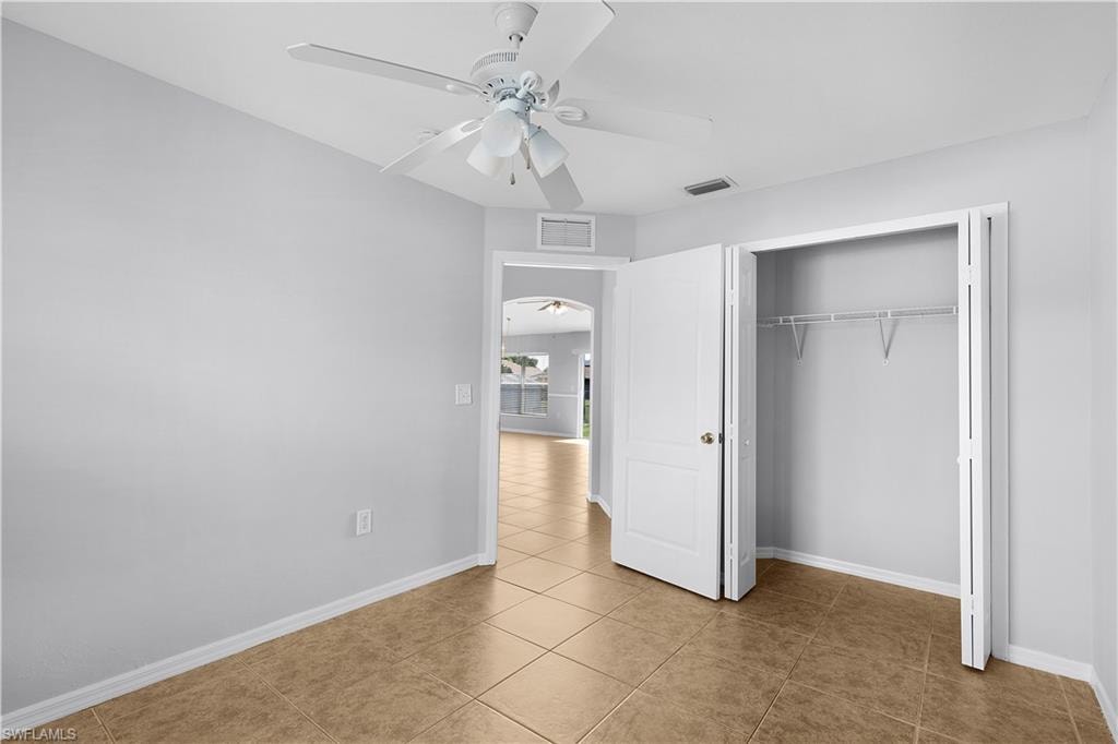 Tile flooring with a neutral finish, a built-in closet with bifold doors, and a ceiling fan with integrated lighting