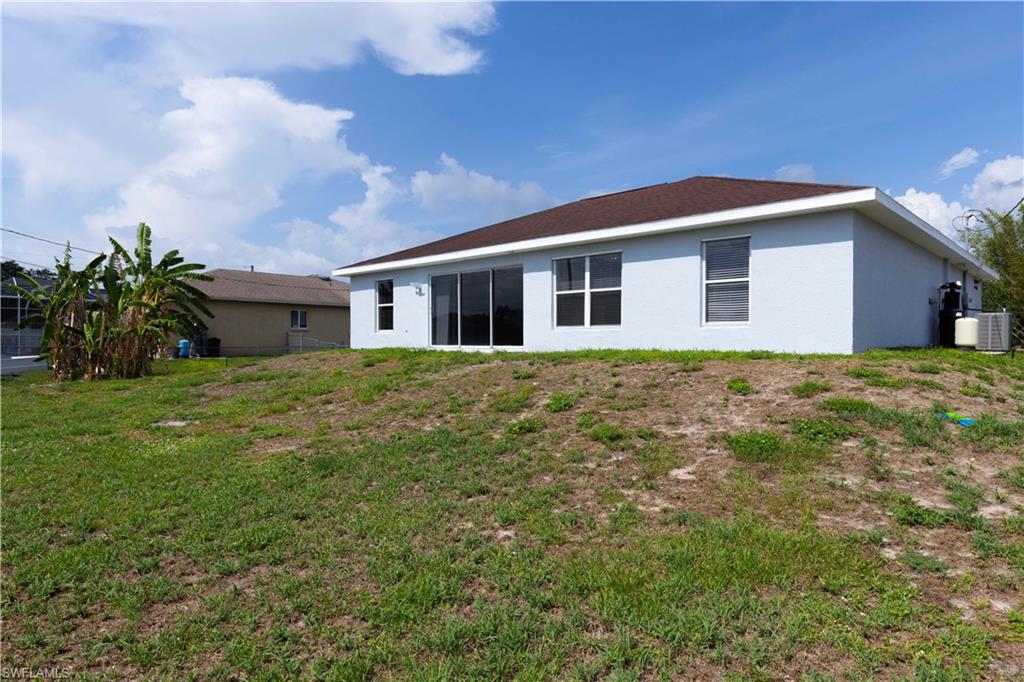 Rear exterior featuring a brown shingle roof, light blue stucco siding, sliding glass doors, and multiple windows