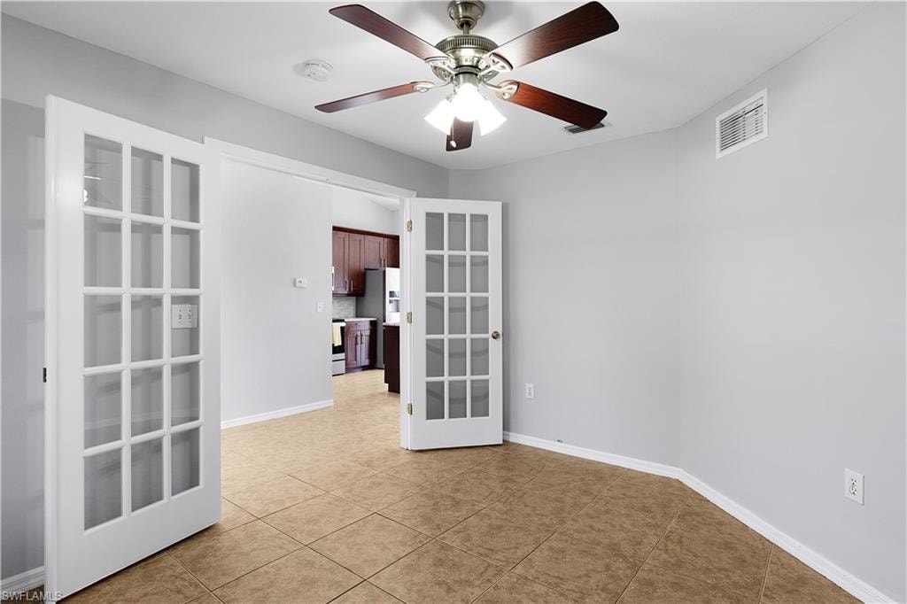 French doors with glass panes, ceiling fan with integrated lighting, tile flooring, and light-toned wall finishes