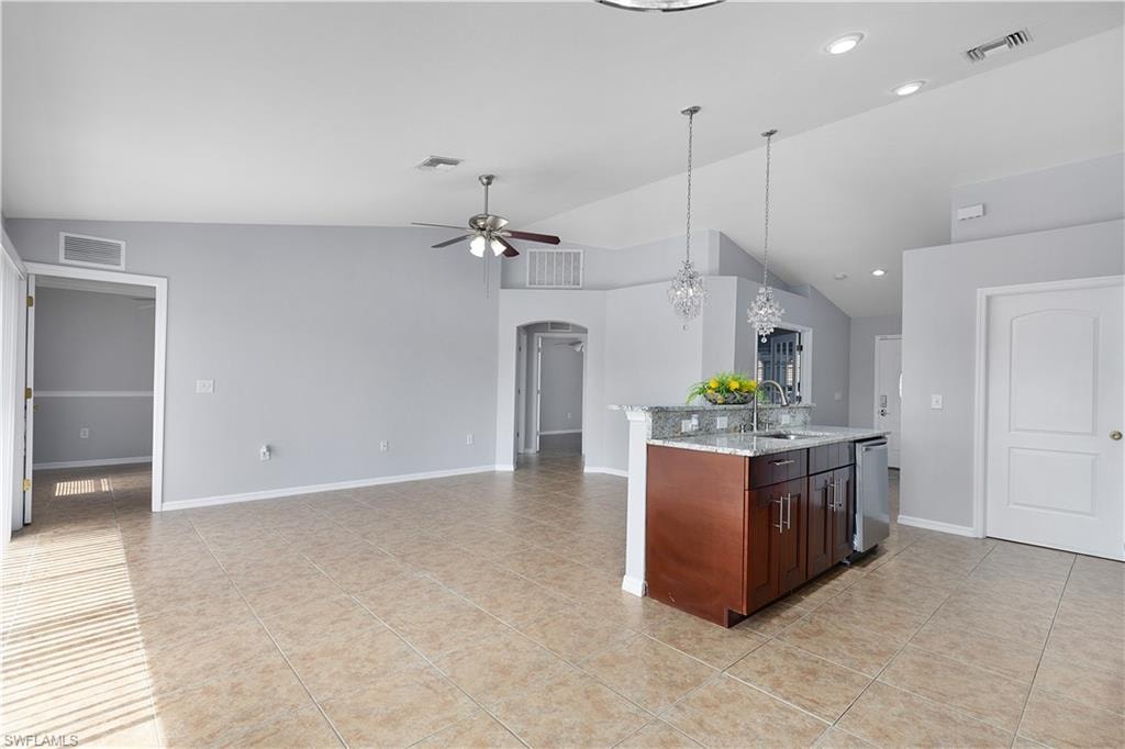 Open-concept living area featuring tile flooring, vaulted ceilings, and a kitchen island with granite countertops