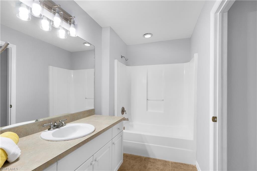 Bathroom featuring a white bathtub/shower combination, vanity with an integrated sink, broad mirror, and a modern light fixture