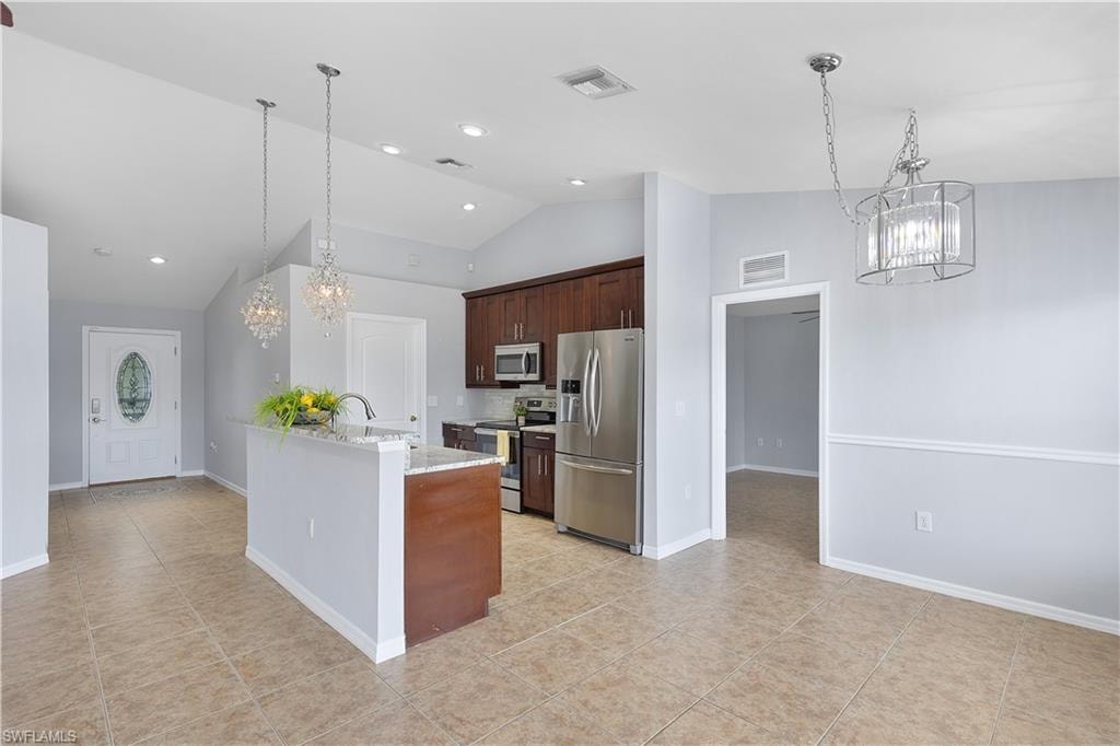 Open-concept kitchen and dining area featuring stainless steel appliances, a two-tone cabinetry design with wood-finish and white painted finishes, granite countertops, a large center island with breakfast bar seating, recessed and pendant lighting, and neutral tile flooring throughout the main living space