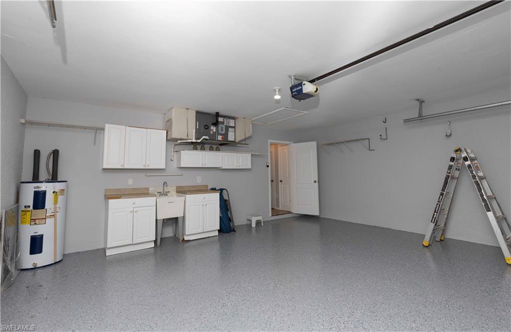 Spacious garage with epoxy-coated flooring, white cabinetry, utility sink, and overhead storage system