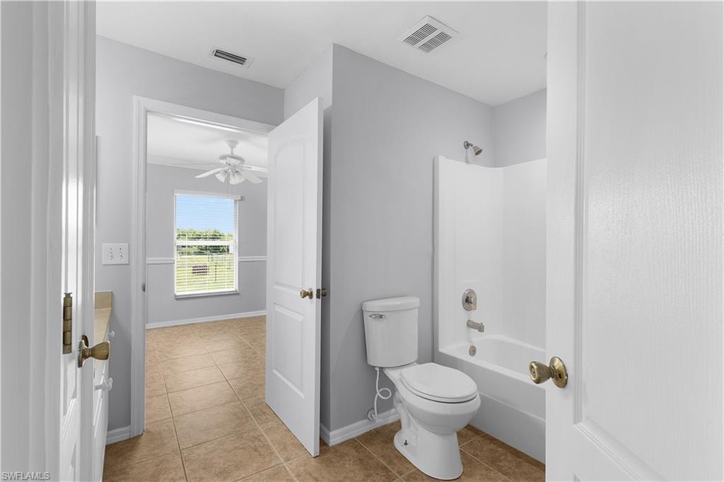 Bathroom featuring a white tub/shower combination, toilet, and tile flooring