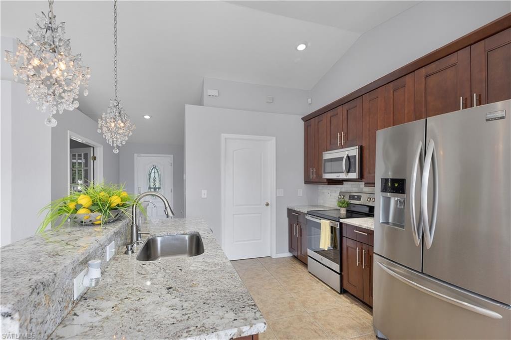 Kitchen featuring granite countertops, stainless steel appliances, wood cabinetry, tile flooring, and vaulted ceiling
