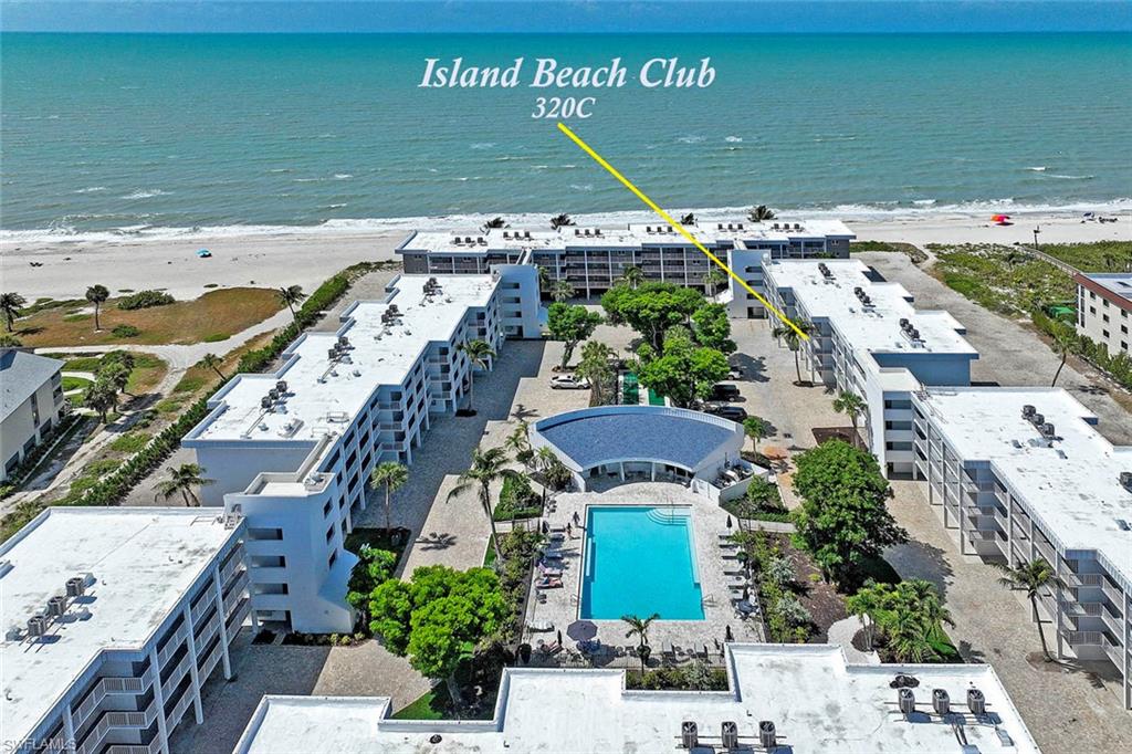 Island Beach Club 320C features a beachfront location with direct oceanfront access, a resort-style heated swimming pool surrounded by mature landscaping, contemporary multi-story residential architecture with clean lines and white exterior finishes, and expansive grounds with hardscaped amenities and green space
