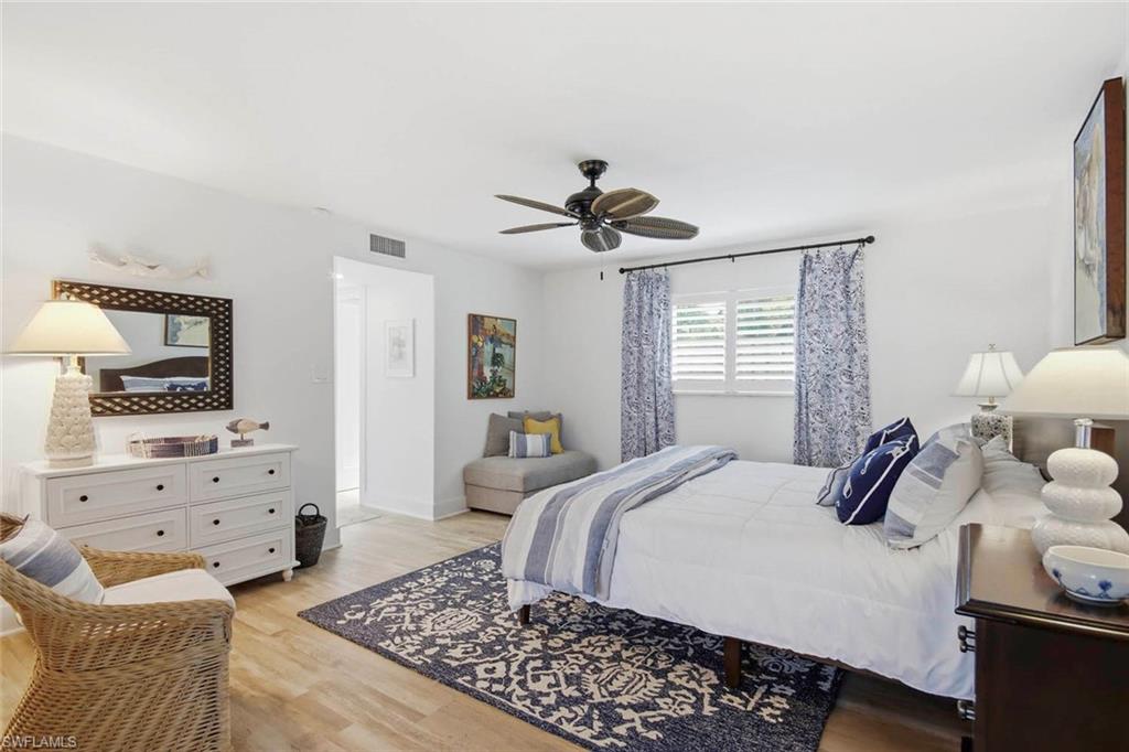 Spacious primary bedroom featuring hardwood flooring, a ceiling fan with remote control, and abundant natural light from shuttered windows