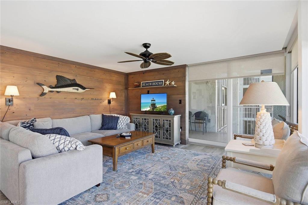 Spacious primary living area featuring wood-paneled accent wall with built-in entertainment cabinetry, ceiling fan, layered lighting with wall-mounted sconces, and direct access to a screened porch