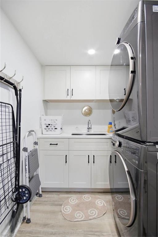 Dedicated laundry room featuring stacked front-load washers and dryers, white shaker-style cabinetry with brushed nickel hardware, quartz countertop with integrated sink, recessed lighting, and wood-finish flooring