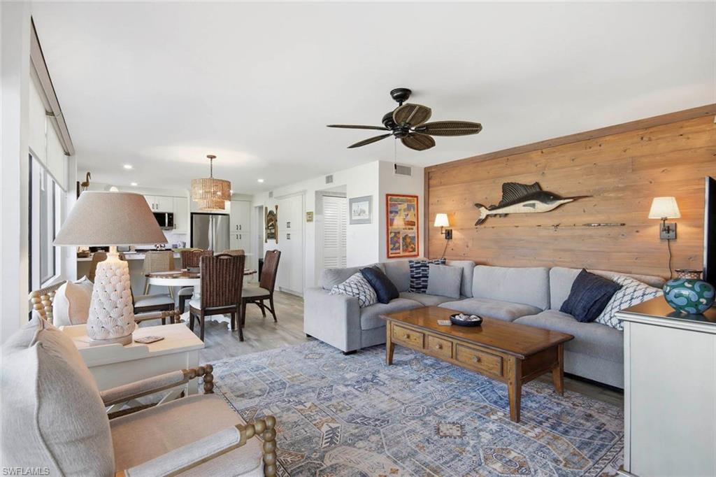 Open-concept living area featuring a wood-plank accent wall, ceiling fan with integrated lighting, recessed ceiling lights, and a wood-finish coffee table with storage drawers