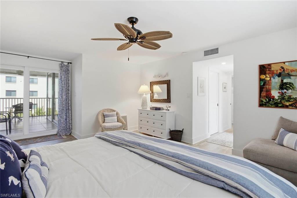 Sliding glass doors opening to an outdoor balcony with metal railing, ceiling fan with natural-toned blades, wide plank flooring, and a white dresser