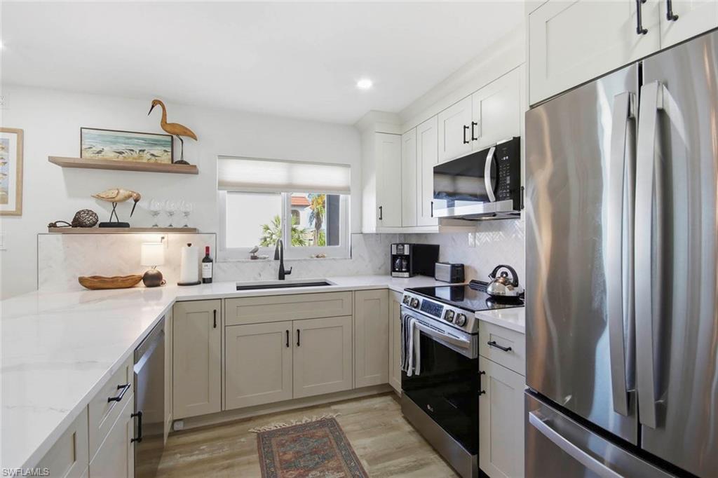 Modern kitchen featuring white cabinetry with brushed metal hardware, quartz countertops, stainless steel appliances including a dual-fuel range and French-door refrigerator, undermount sink with chrome faucet, and wood-finish flooring throughout