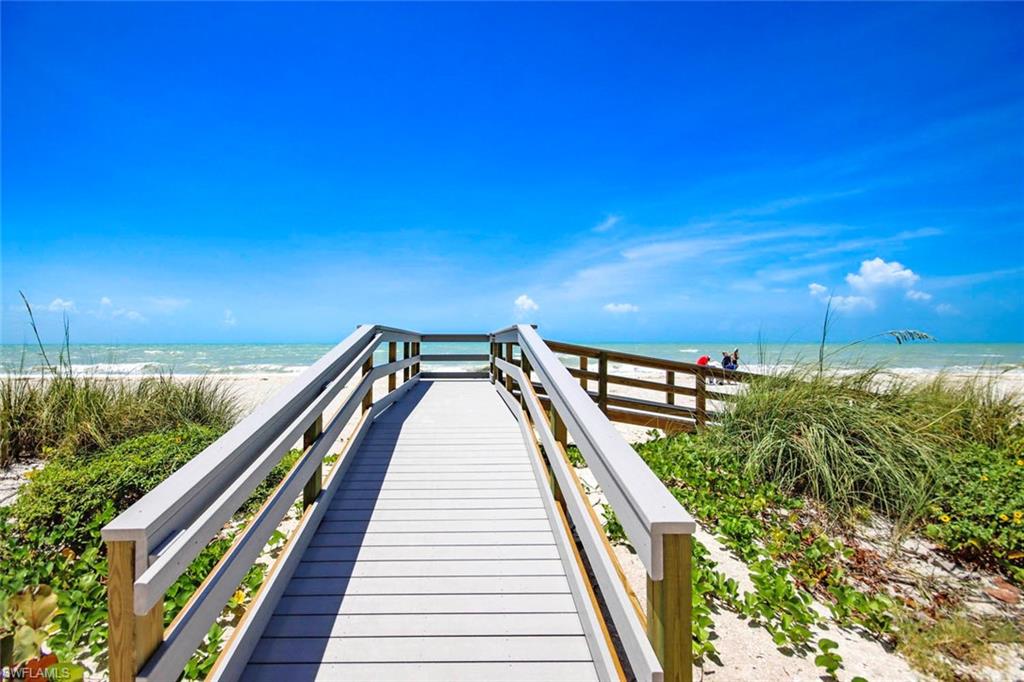 Coastal boardwalk featuring composite decking with sturdy wood-finish railings, leading through native dune vegetation to pristine sandy beach
