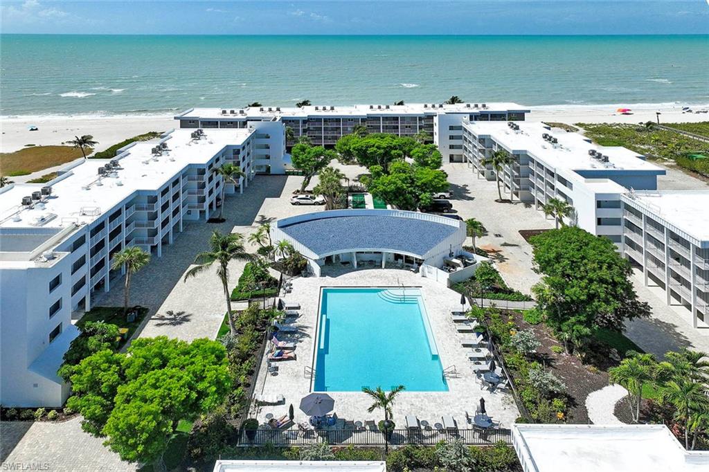 Expansive beachfront property featuring multiple buildings with balconies, a large outdoor swimming pool, and mature landscaping