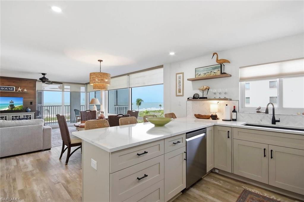 Open-concept kitchen and dining area featuring a large white quartz island with storage drawers, stainless steel appliances including a dishwasher, soft-close cabinetry with matte black hardware, and hardwood-finish flooring throughout