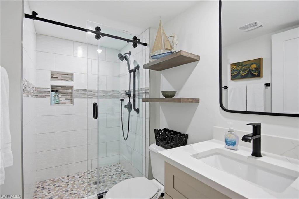 Spa-inspired primary bathroom featuring a frameless glass-enclosed shower with rainfall showerhead and hand-held spray, white subway tile surround, and pebble-finish floor
