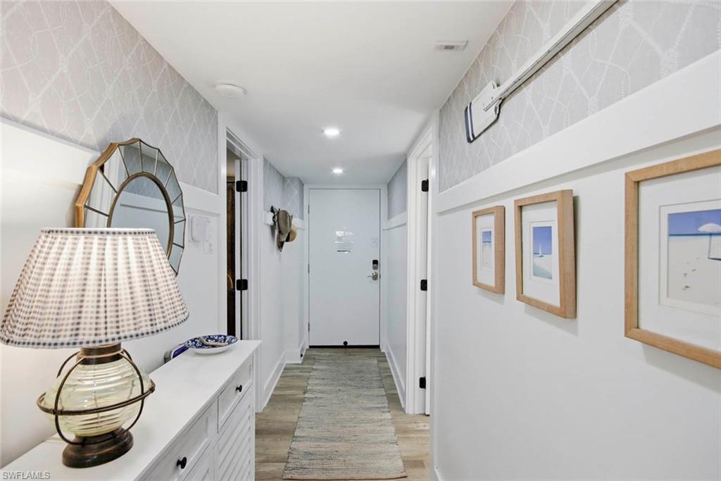 Bright hallway featuring white shaker cabinetry with hardware accents, wood-finish flooring, recessed ceiling lighting, and framed coastal artwork