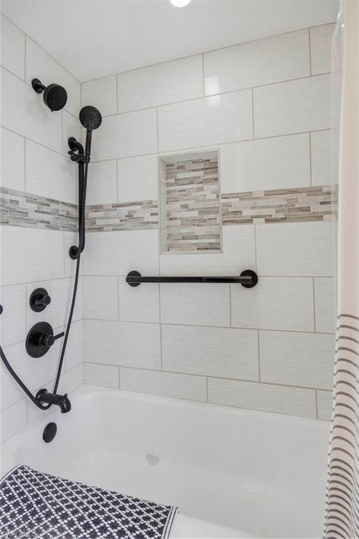 Spa-inspired shower featuring large-format white subway tile walls, a decorative mosaic tile accent band, dual showerheads with handheld spray, matte black fixtures and hardware, and a textured floor surface for enhanced safety and traction