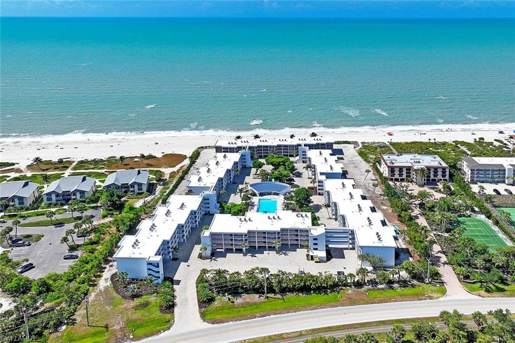 Beachfront resort-style community featuring multiple residential buildings with contemporary architecture, a central courtyard with resort-style pool and spa, manicured landscaping with mature trees, and direct beach access overlooking the Atlantic Ocean