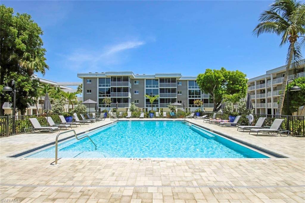 Resort-Style Pool Oasis with Sparkling Turquoise Waters, Spacious Sundeck Featuring Lounge Seating, Mature Landscaping with Palm and Shade Trees, Multi-Story Residential Buildings with Modern Balconies, and Meticulously Paved Patio Surround