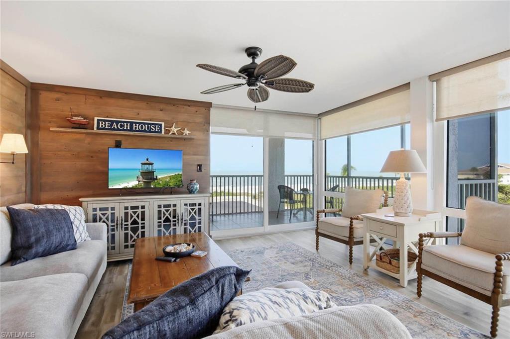 Spacious master suite with wood-paneled accent wall, ceiling fan with integrated lighting, and expansive glass doors opening to a covered balcony with ocean and landscape vistas