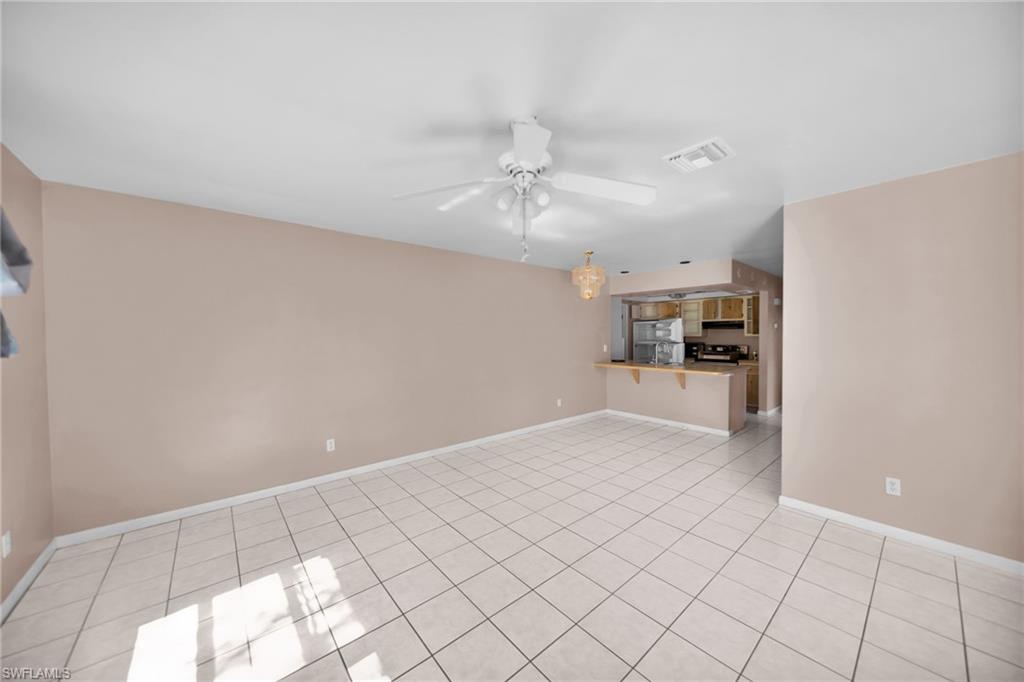 Spacious open-concept living area featuring diagonal tile flooring, ceiling fan with integrated lighting, and pass-through kitchen with cabinetry and appliance cutouts