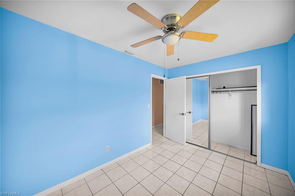 Bright bedroom showcasing vibrant blue walls, ceramic tile flooring, ceiling fan with wood-finish blades, and a mirrored sliding-door closet with interior shelving and hanging rod