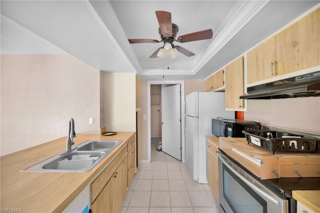 Galley kitchen featuring wood-finish cabinetry, a stainless steel double basin sink, and tile flooring