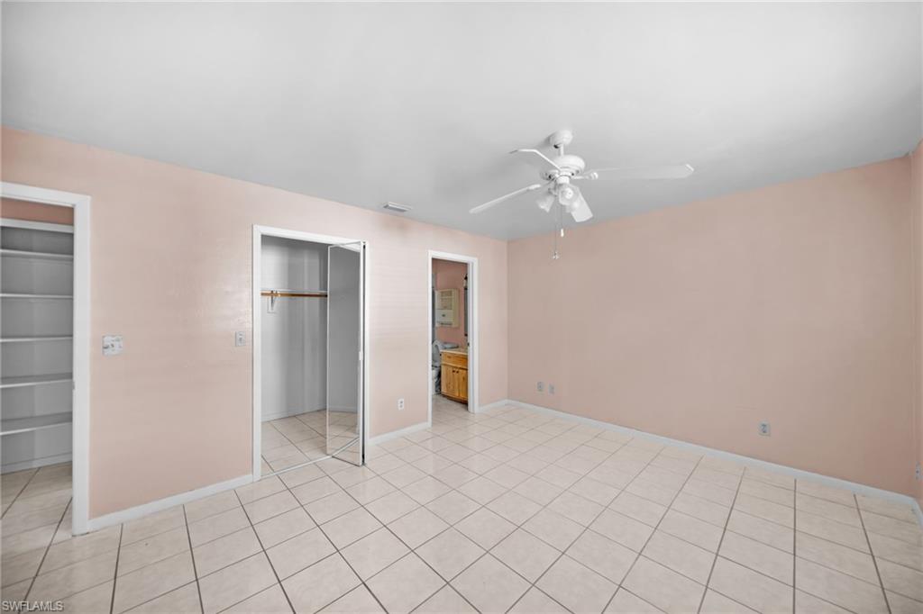 Spacious room featuring tile flooring throughout, soft pink walls, a ceiling fan, and multiple closet spaces including a reach-in closet with sliding glass doors