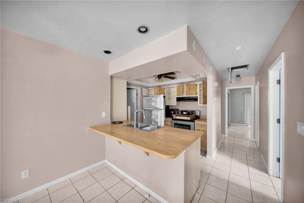 Open kitchen with wood-finish countertop pass-through, stainless steel appliances, and tile flooring throughout
