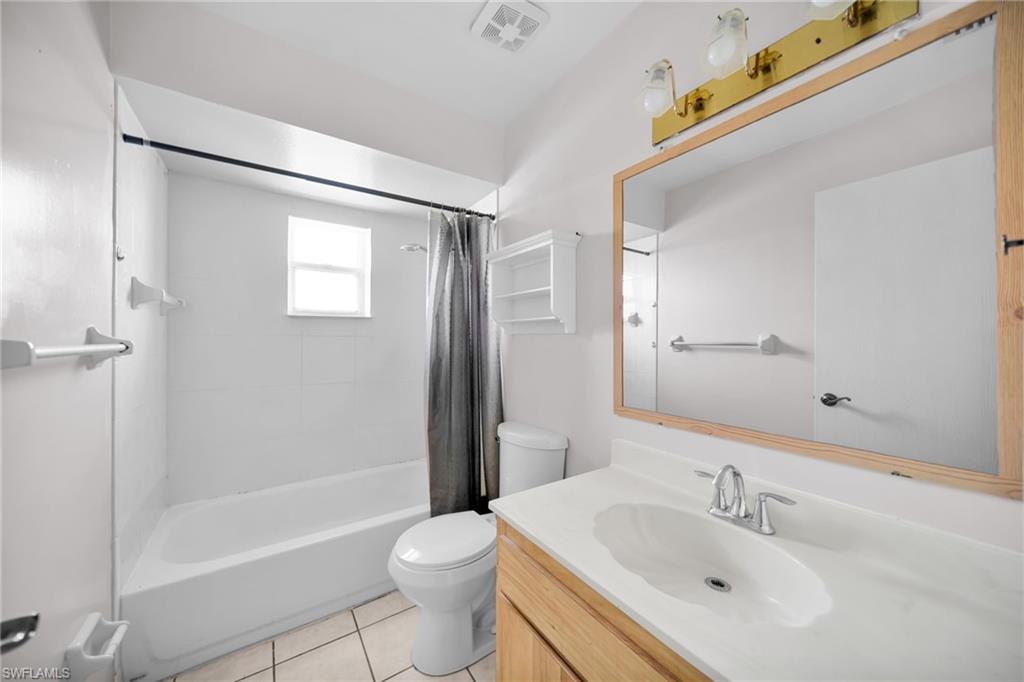 Bathroom featuring a white bathtub, tiled shower surround, window, wood-finish vanity, and a large framed mirror