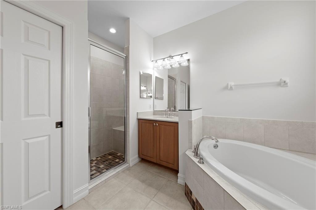 Spa-inspired primary bathroom featuring a wood-finish vanity with dual sinks, quartz countertop, and polished chrome fixtures