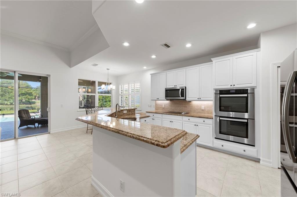 Gourmet kitchen featuring white cabinetry, dual wall-mounted ovens, stainless steel appliances, and a large center island with stone countertops