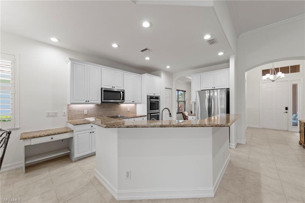 Gourmet kitchen featuring white cabinetry, granite countertops, stainless steel appliances including a built-in refrigerator and double wall ovens, a spacious island with breakfast bar seating, recessed lighting throughout, and light wood-finish flooring that extends into the adjoining open-concept living areas