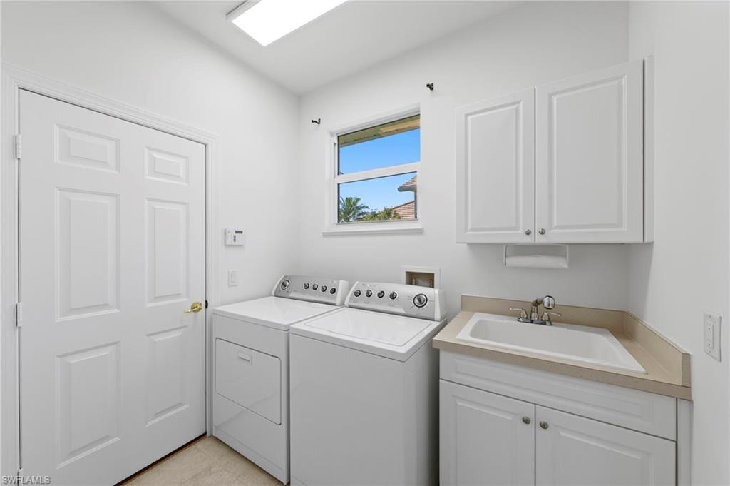 Dedicated laundry room featuring side-by-side washer and dryer, white cabinetry with wood-finish countertops, stainless steel sink with faucet, ample storage, skylight, and a window with natural light