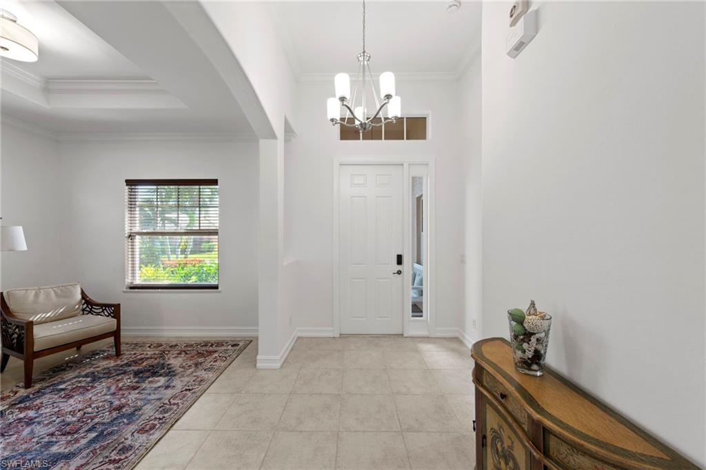 Bright foyer showcasing neutral tile flooring, white painted walls, and a pendant light fixture suspended from a coffered ceiling