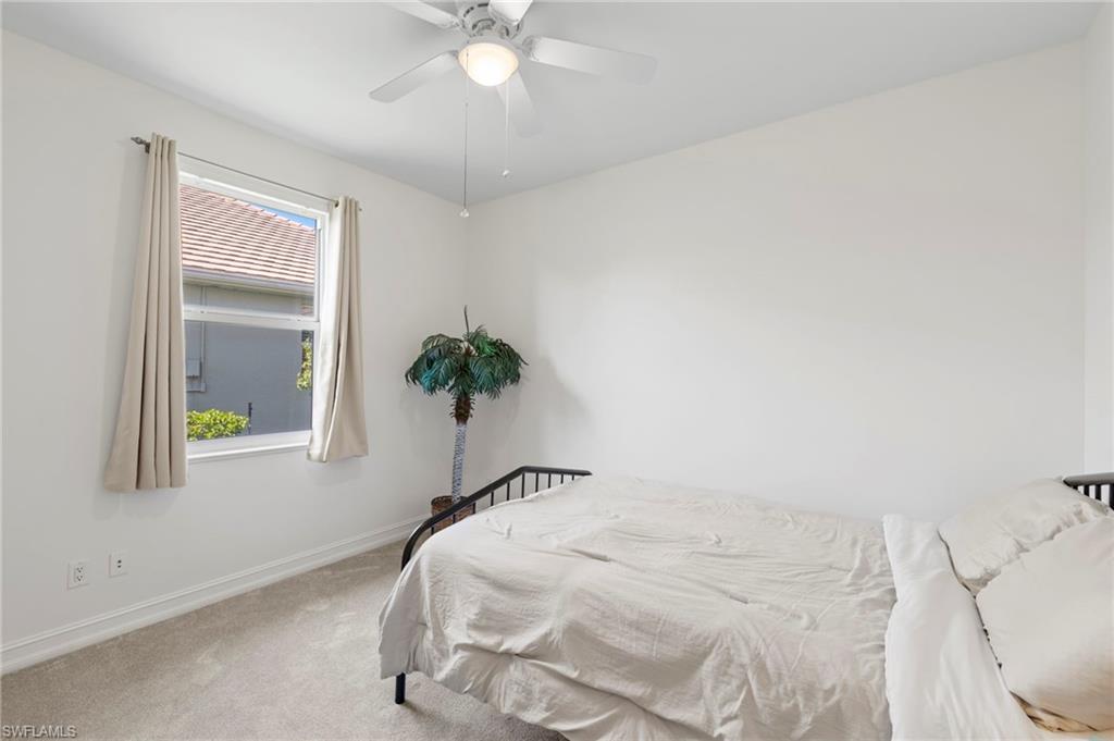 Bright secondary bedroom featuring neutral carpeting, ceiling fan with integrated lighting, and large window with natural light exposure