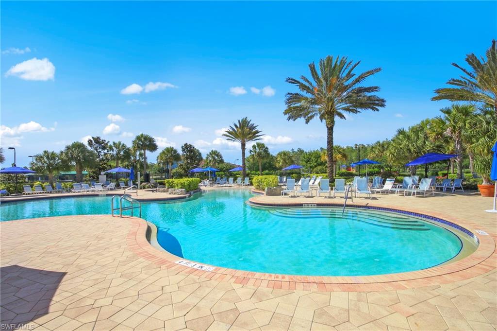 Expansive resort-style pool with multiple swimming areas, a textured paver deck, and surrounding mature palm trees