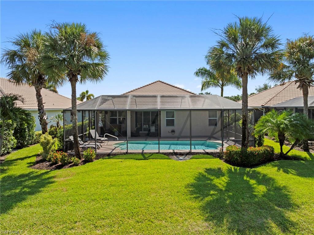 Expansive backyard oasis featuring a resort-style screened pool with hardscape decking, mature palm trees, and lush manicured lawn
