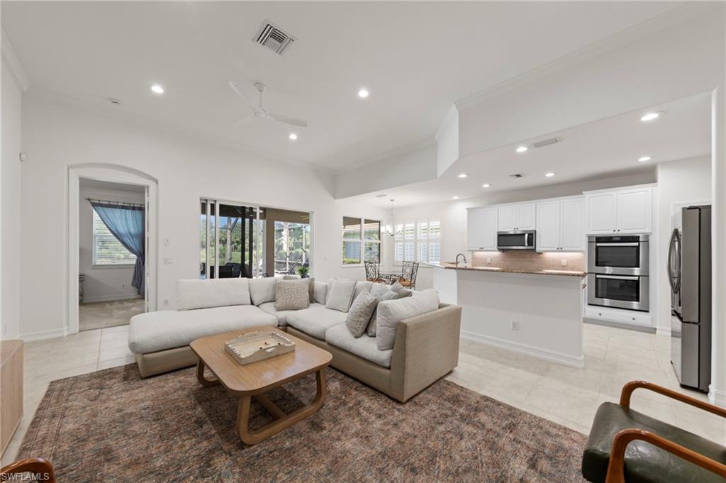 Open-concept living and kitchen area featuring recessed ceiling lighting, a neutral color palette, stainless steel appliances including a built-in wall oven and microwave, white cabinetry with wood-finish countertops, and a wood-finish coffee table anchoring the seating area