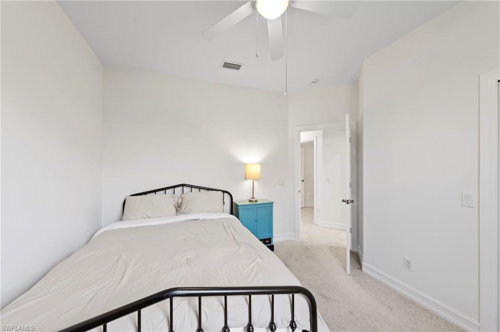 Bright secondary bedroom with metal frame bed, neutral carpeting, ceiling fan with integrated lighting, and direct access to ensuite bathroom