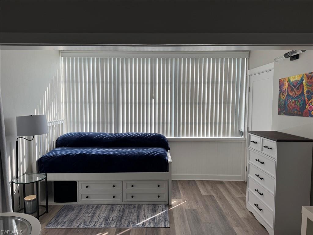 Window with vertical blinds, wood-finish flooring, white walls, and a built-in storage bed frame