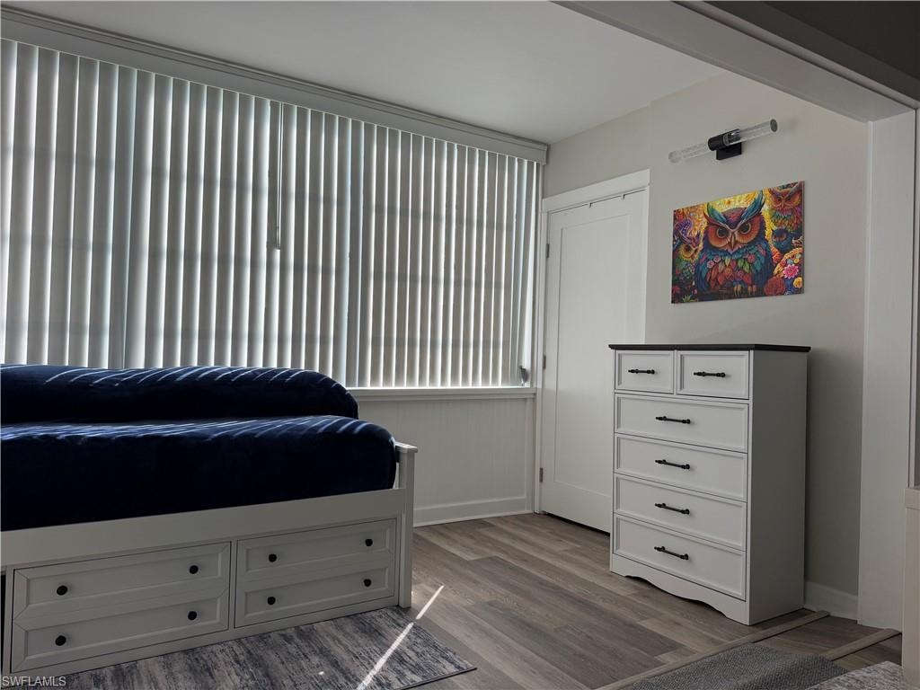 Vertical window blinds, wood-finish flooring, white door, wall-mounted light fixture, and crown molding