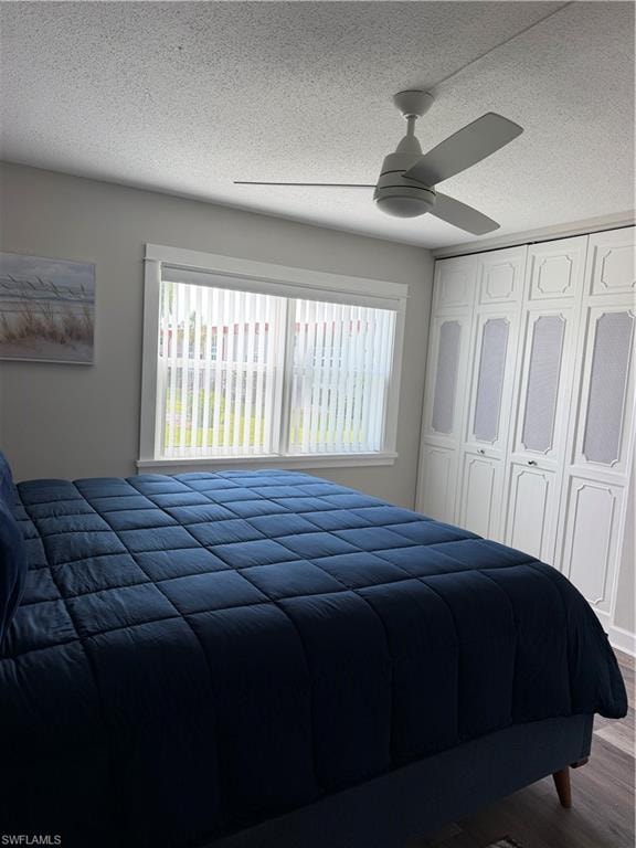 Built-in wardrobe storage, neutral ceiling fan, white window trim, and wood-finish flooring