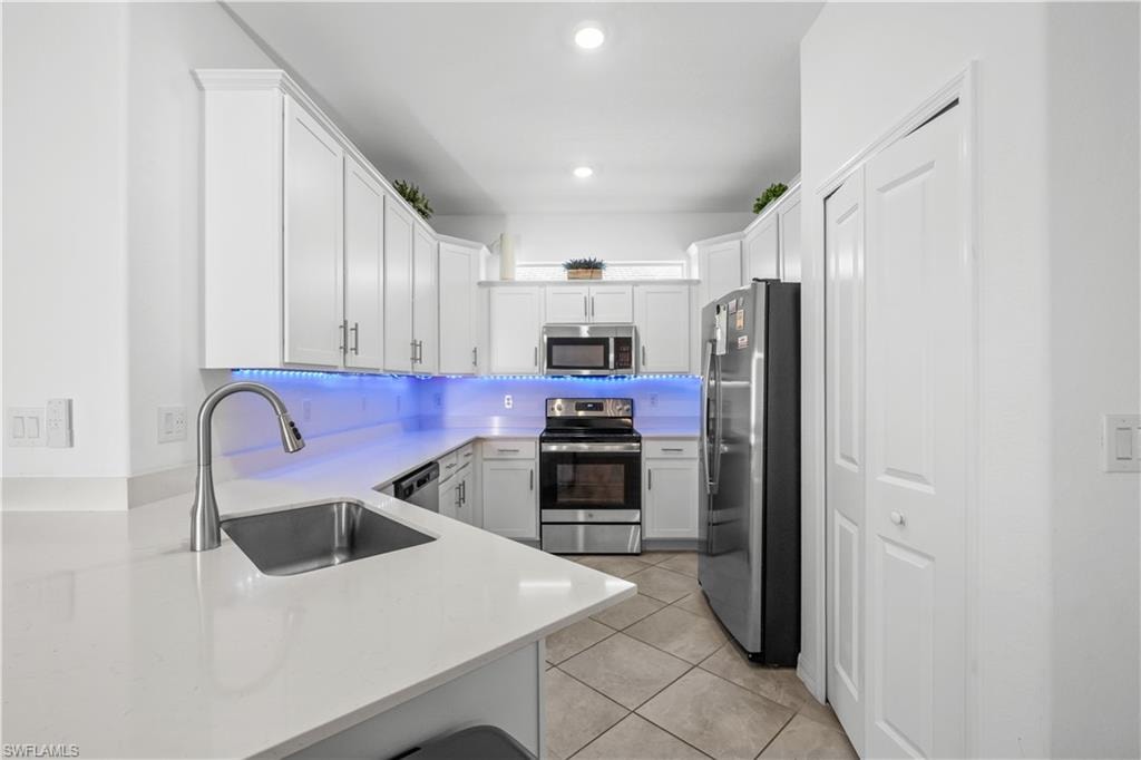 Contemporary kitchen featuring stainless steel appliances, white cabinetry, a single basin sink with a gooseneck faucet, light-toned countertops, and tile flooring