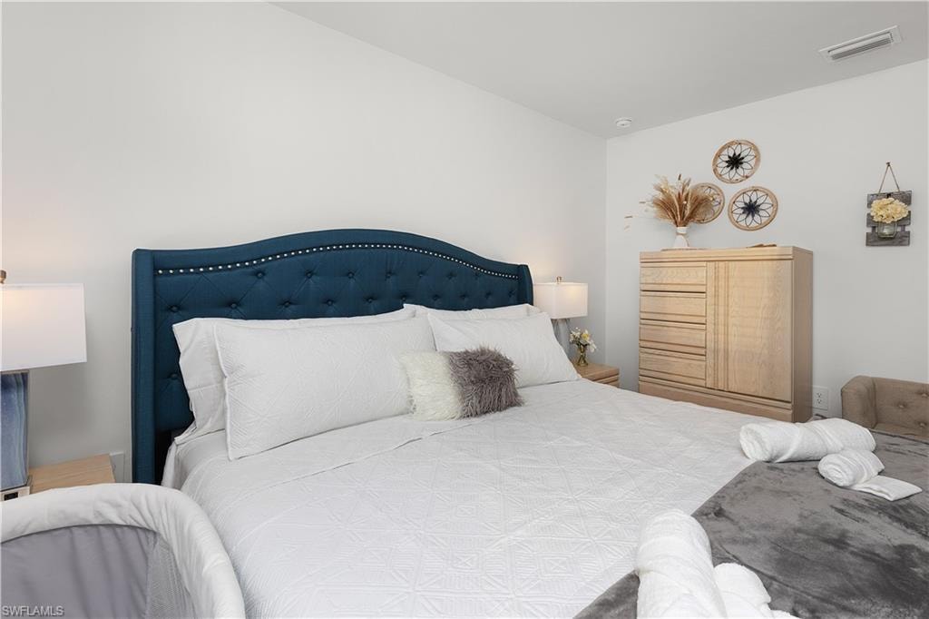Accent wall featuring a tufted upholstered headboard with nailhead trim, flanking bedside tables, and a light-toned wooden dresser
